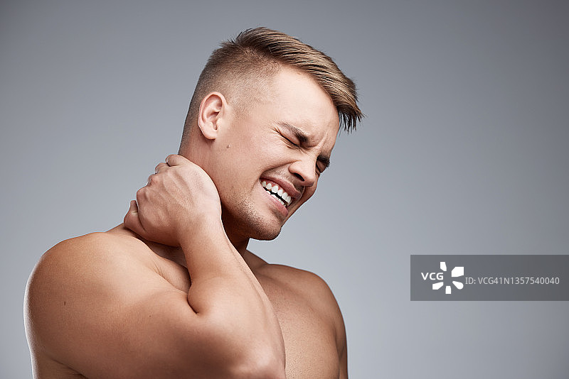 工作室拍摄了一个肌肉发达的年轻人在灰色背景下经历脖子疼痛图片素材
