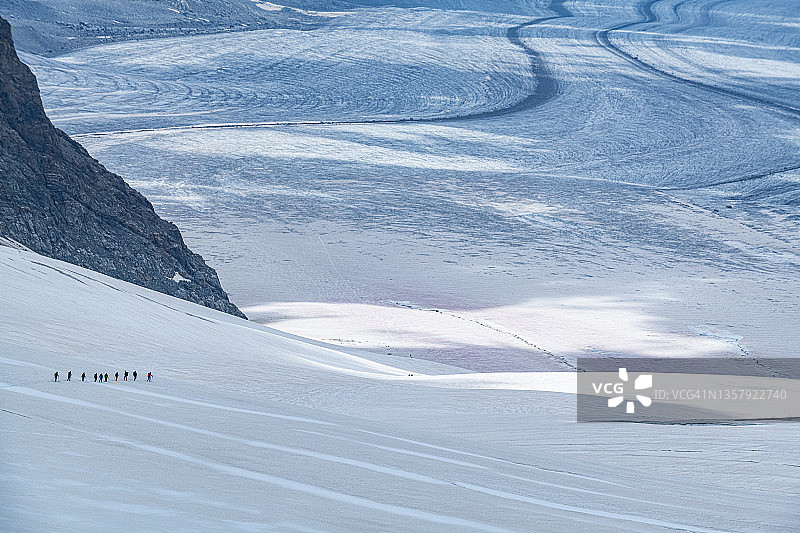 徒步旅行者在阿莱奇冰川的大雪中行走的剪影图片素材