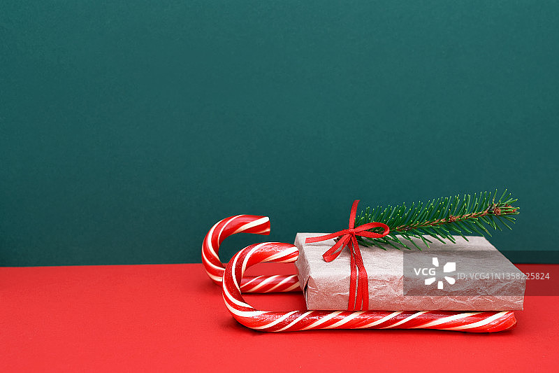 圣诞老人的自制雪橇，由红色和白色条纹糖果在一根手杖的形式和一个礼品盒与一个红色丝带蝴蝶结和一个云杉树枝，传递祝贺和礼物给家人和朋友，复制空间。图片素材