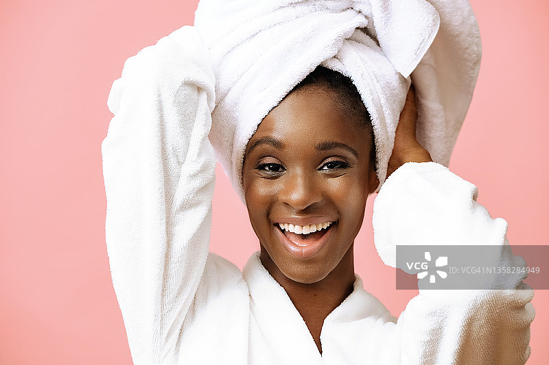 年轻美丽的女人在浴衣与白色毛巾在头上摆在粉红色的背景图片素材