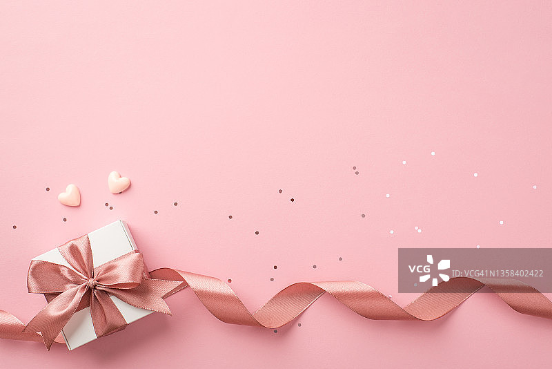 俯视图照片的情人节装饰白色礼品盒蝴蝶结粉红色的卷丝带小的心和亮片在孤立的淡粉色背景与空的空间图片素材