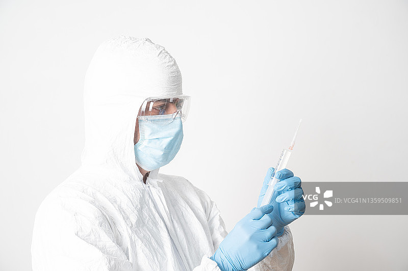 一名科学家手持一种抗冠状病毒的疫苗并进行检测。ο突变包括在内。他戴着防护面罩、眼镜和防护服。图片素材