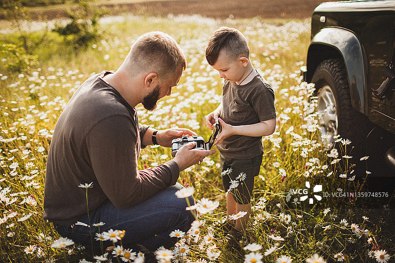 父亲教儿子在户外美丽的大自然中用旧胶卷相机拍照图片素材