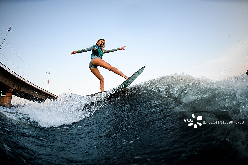 美丽迷人的女人平衡在巨大的飞溅的波浪在wakesurf。图片素材