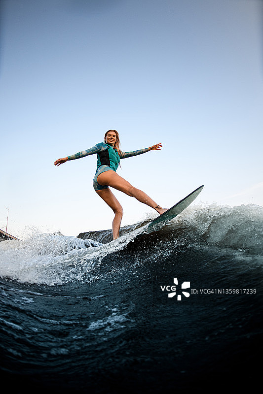 迷人的微笑的女人平衡在飞溅的波浪在wakesurf。图片素材