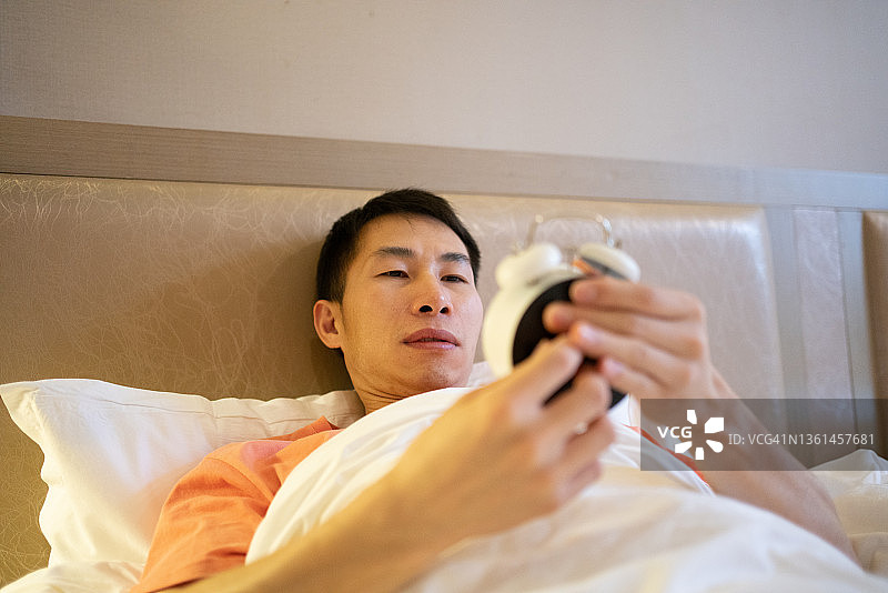 亚洲人躺在床上，手里拿着闹钟图片素材