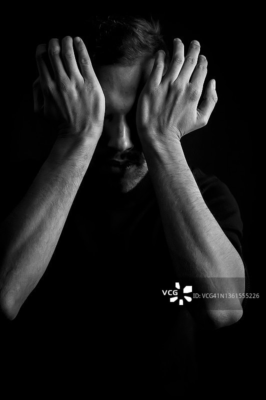 一个年轻人的黑白肖像，他用手掌遮住眼睛，以免被光线干扰图片素材