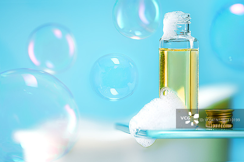 美容产品泡沫肥皂，沐浴露或洗发水和飞行的肥皂泡沫在流行的蓝色背景。图片素材