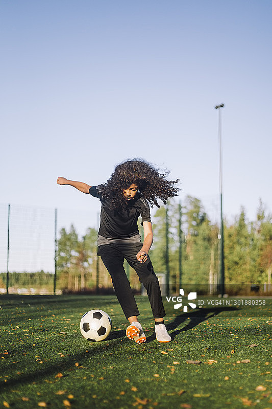 女孩在阳光明媚的日子里在运动场上踢足球图片素材