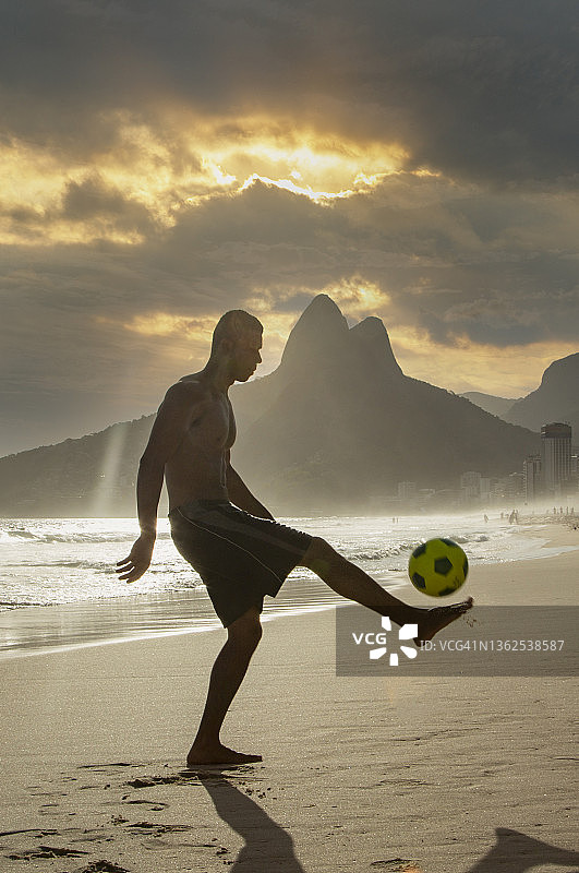 一个男人在沙滩上踢足球图片素材