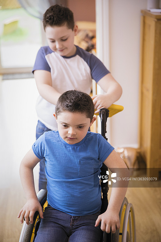 男孩推着轮椅上患有唐氏综合症的弟弟图片素材