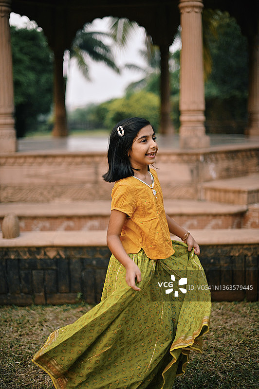 穿着传统服装的印度女孩在一个圆顶建筑前纺纱图片素材