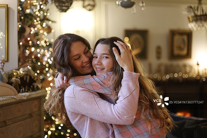 母亲和她的女儿在圣诞树前拥抱图片素材
