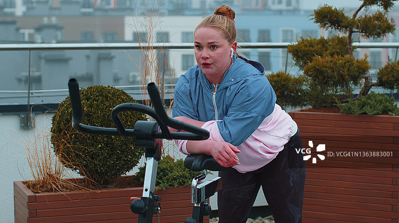 运动女孩进行有氧骑行训练练习在自行车固定自行车上的屋顶图片素材