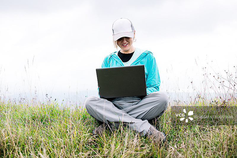 一个成年女人坐在草地上用她的笔记本电脑图片素材