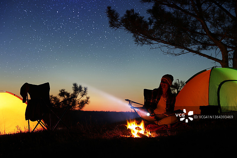 晚上拿着手电筒在篝火旁的女人。露营的季节图片素材