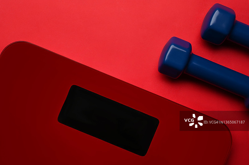 红色背景上的数字秤和哑铃。减肥和健康的生活方式理念。图片素材