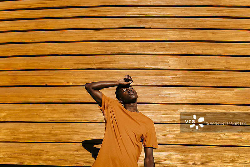一个年轻人闭着眼睛站在橘黄色的墙前图片素材