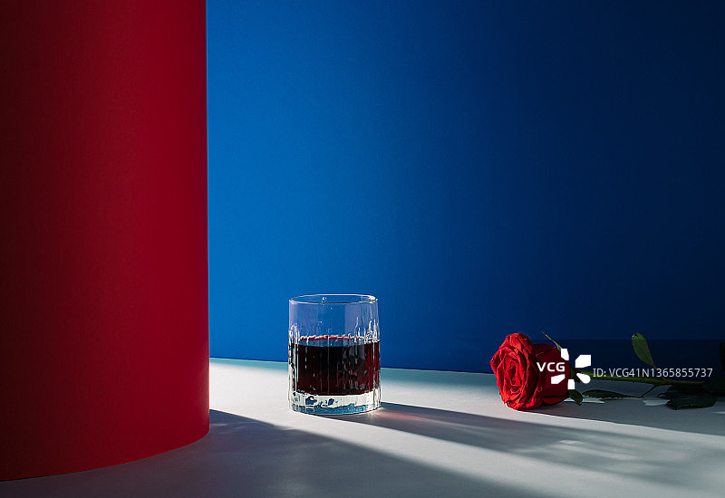 由一杯饮料和一朵红玫瑰组成的创意浪漫安排。蓝色和红色的背景与光和阴影。最小的爱的概念。情人节的灵感。图片素材