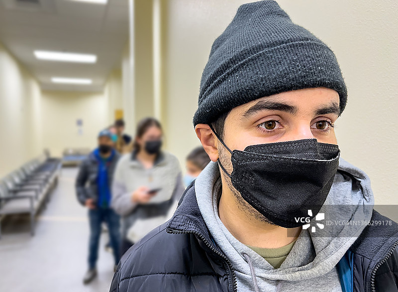 年轻的西班牙裔男子戴着防护口罩排队接种疫苗图片素材