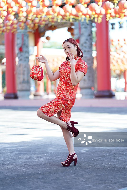 亚洲中国妇女穿着旗袍，拿着购物袋。图片素材
