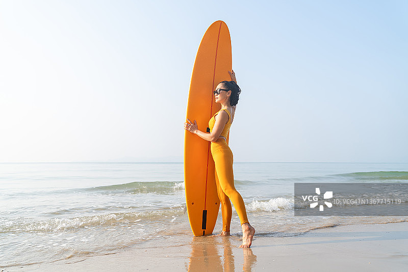 女性冲浪手在沙滩上举着冲浪板的肖像图片素材