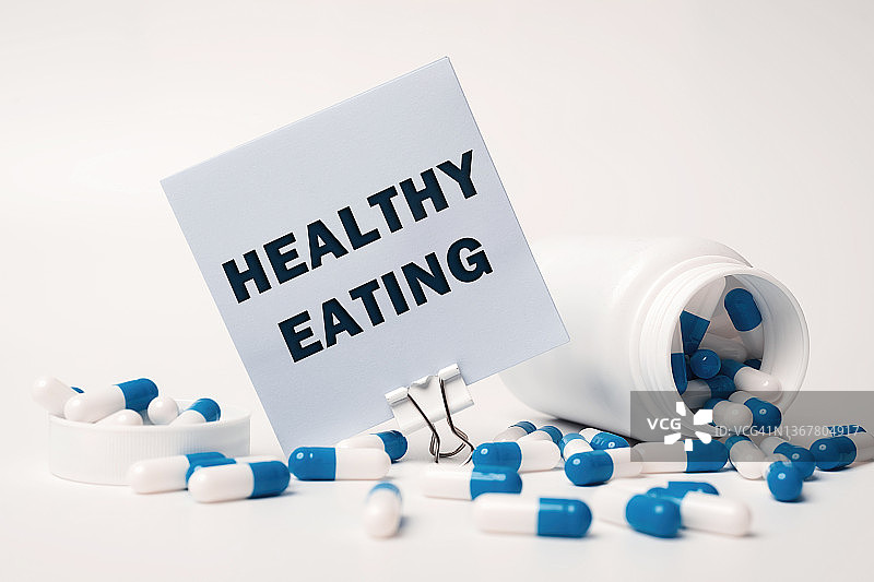 文字——健康饮食，写在从药瓶里溢出的蓝白色药丸旁边的便利贴上。医学的概念图片素材