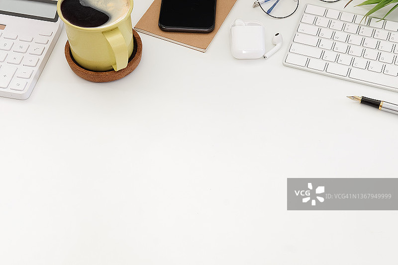 白色办公桌上的咖啡、智能手机、计算器和无线键盘。图片素材