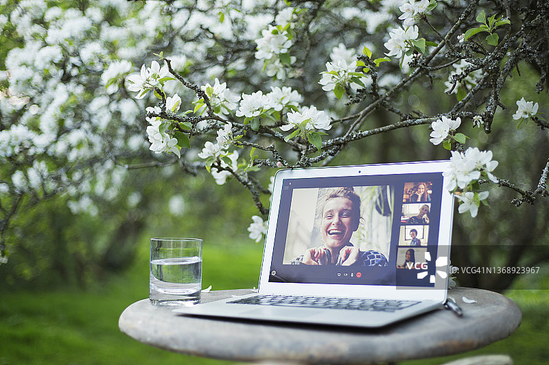 在花园的花树下，朋友们在笔记本电脑屏幕上视频聊天图片素材