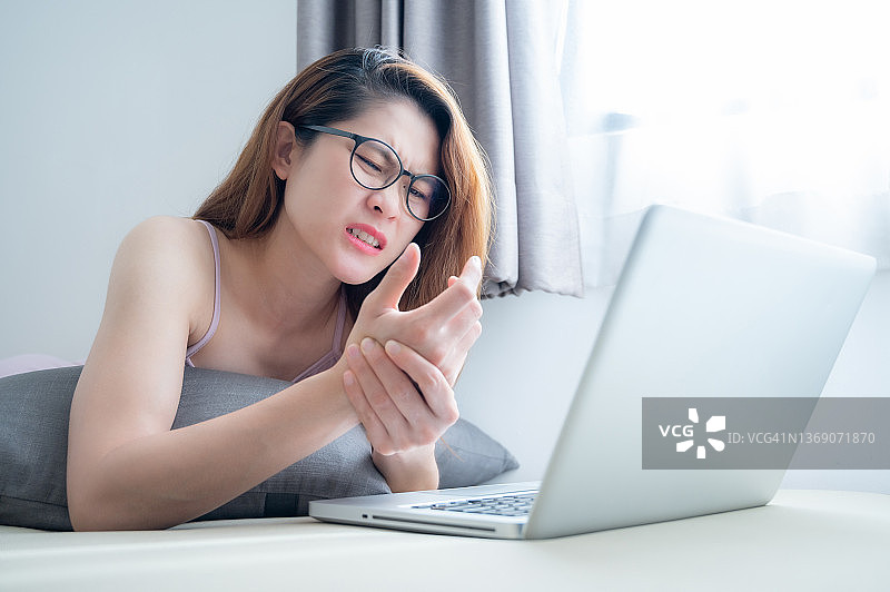 年轻的亚洲女性因使用电脑工作或长时间保持同一姿势而导致手腕疼痛。图片素材