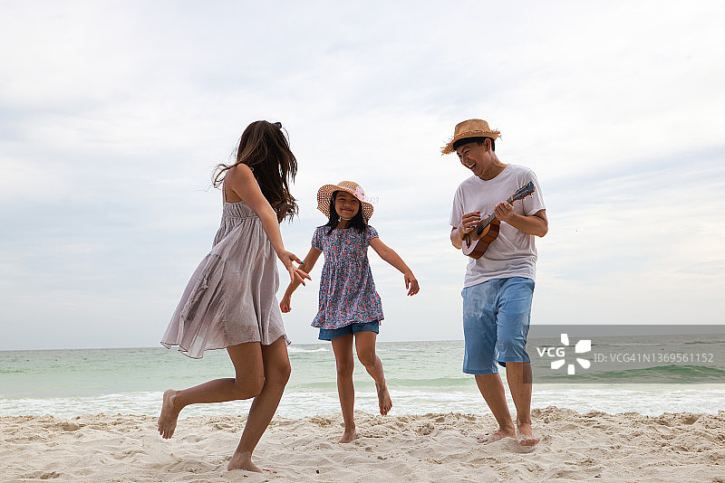 快乐的家庭爸爸妈妈和女儿一起在海边玩音乐跳舞，暑假概念图片素材