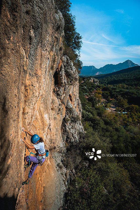 攀登者攀爬郁郁葱葱的山谷上陡峭的岩壁图片素材