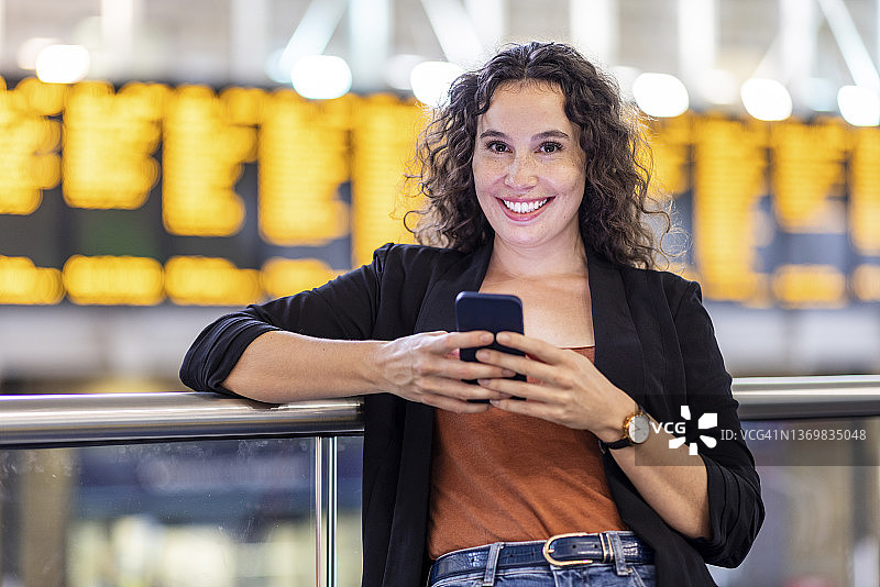 微笑的年轻女子在火车站拿着智能手机图片素材