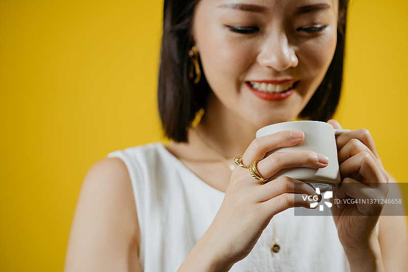 年轻美丽的亚洲女子端着一杯咖啡，配以金戒指、耳环、项链、手镯等奢华配饰图片素材