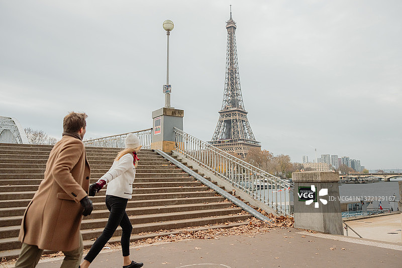 女人迫不及待地想看艾菲尔铁塔，和男朋友手牵着手朝铁塔方向跑去图片素材