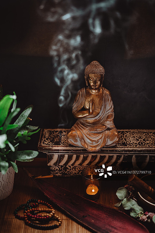 低调的静物画的是一尊金佛雕像，里面有一根冒烟的熏香，一根点燃的蜡烛，一个唱歌的碗，念珠和一个豆荚里的绿色植物图片素材