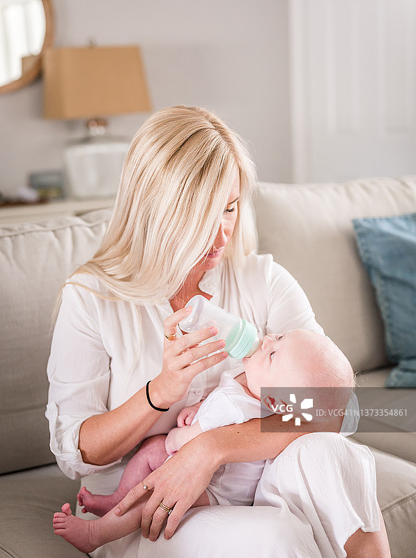 母亲抱着刚出生的儿子，在家里用奶瓶喂他图片素材