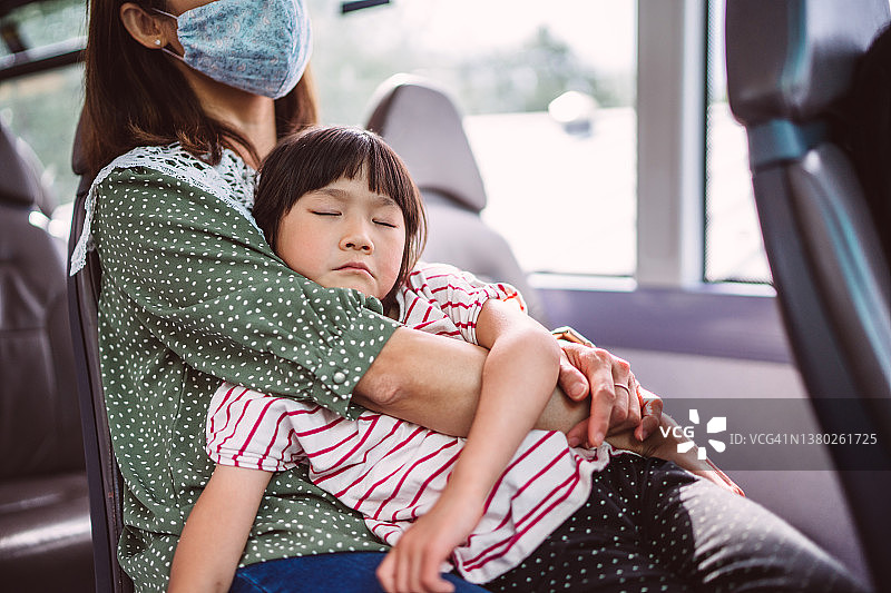 一个疲惫的小女孩在公交车上睡在妈妈的怀里图片素材