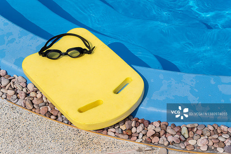 游泳池旁边有一块带护目镜的黄色游泳板。图片素材