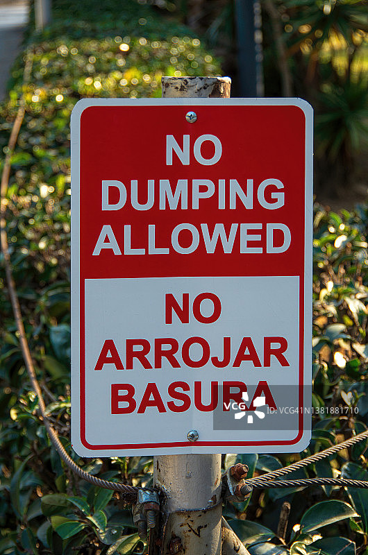 一个城市公园旁边用英语和西班牙语写着“禁止倾倒/禁止倾倒”的双语标志图片素材