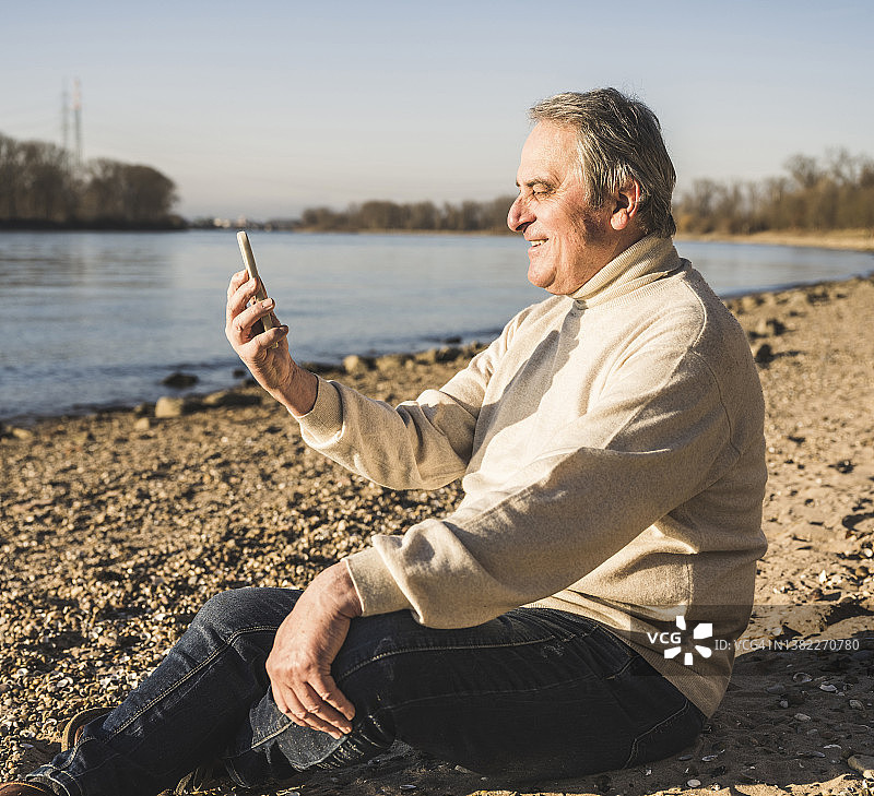 在阳光明媚的日子里，快乐的老人通过手机在海滩上做视频通话图片素材