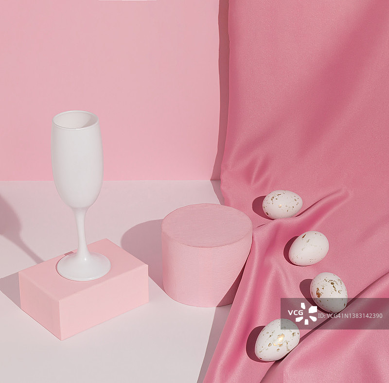 淡粉色的复活节构图，配以酒杯、绸缎窗帘和白鸡蛋。适合产品展示和经营理念。现代美学。复活节快乐。图片素材