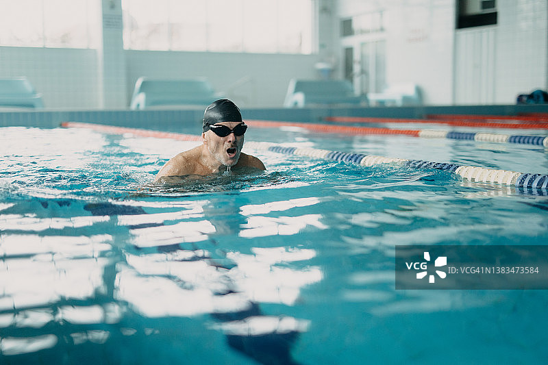 活跃的高级男子游泳运动员在室内游泳池游泳。图片素材