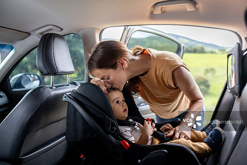 慈爱的母亲在汽车的安全座椅上亲吻她的儿子图片素材