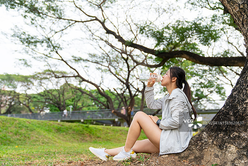 亚洲妇女在公园晨跑时喝瓶装水。图片素材