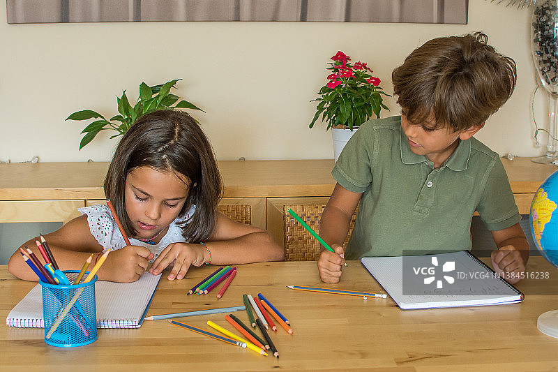 6岁的男孩和女孩在家里的客厅里做作业。图片素材