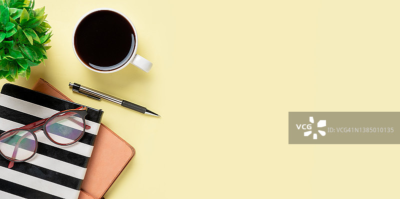 带眼镜的办公桌，钢笔，笔记本，黄色背景的咖啡杯图片素材