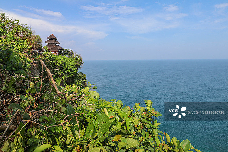 印度尼西亚巴厘岛，乌鲁瓦图悬崖、凉亭和蔚蓝的大海。白天，Pura Luhur Uluwatu寺庙景色优美，前景是五颜六色的花朵。风景优美，海岸景观悬崖高。图片素材