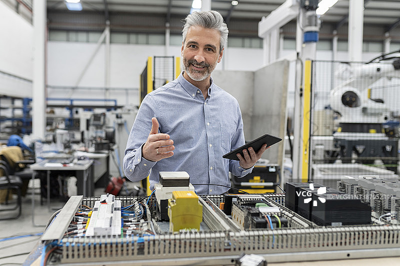 微笑的工程师拿着平板电脑站在工厂的机器旁边图片素材