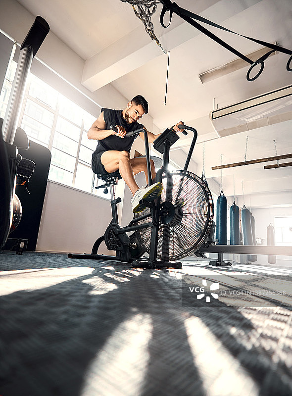 低角度拍摄的一个运动的年轻人在健身房里锻炼自行车图片素材